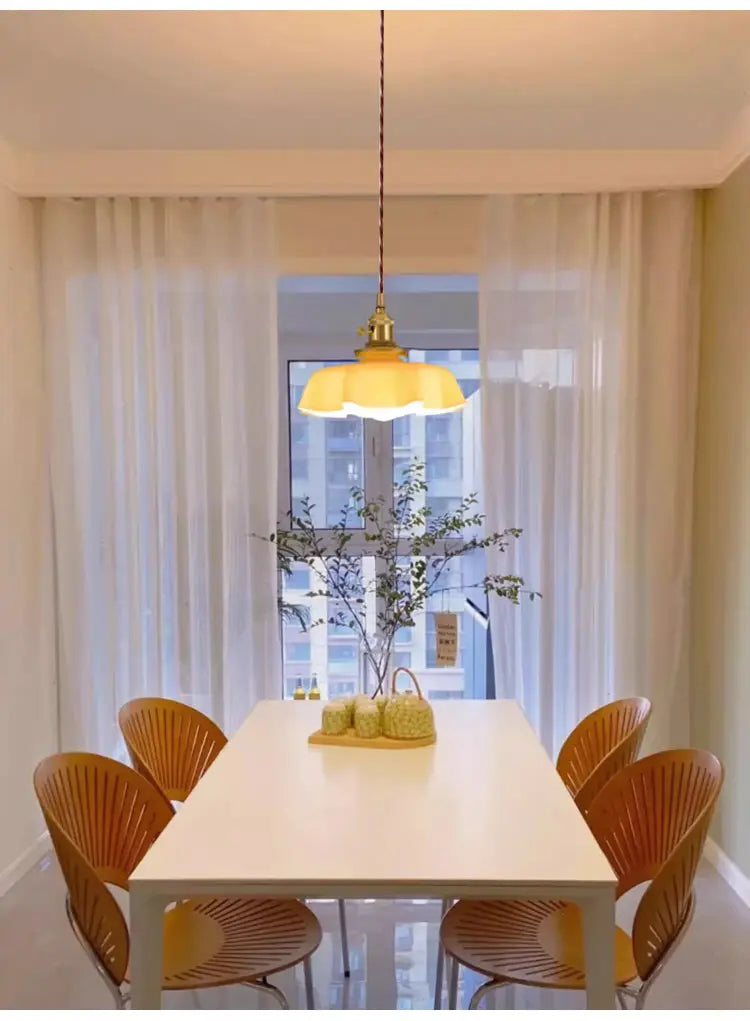 Un luminaire suspendu à jupe florale en verre jaune légèrement chaud avec une tête de lampe en cuivre et un support à finition laiton suspendu au plafond, vu depuis le dessous.