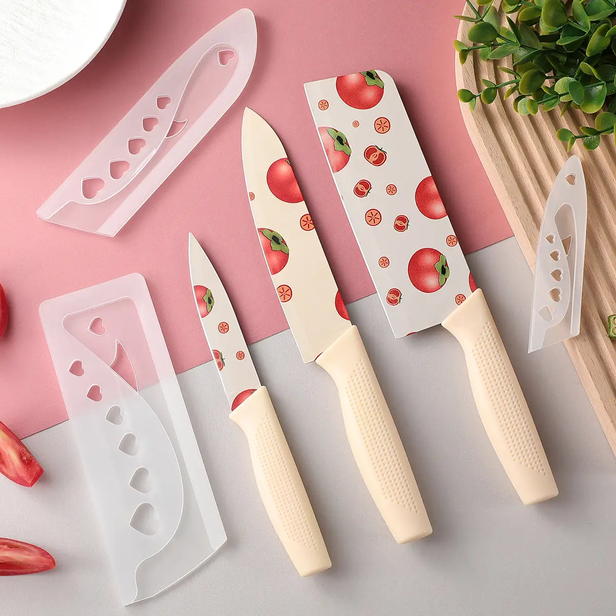 Set of three ceramic kitchen knives with tomato-themed blades and cream-colored textured handles each with a matching translucent heart-patterned sheath.