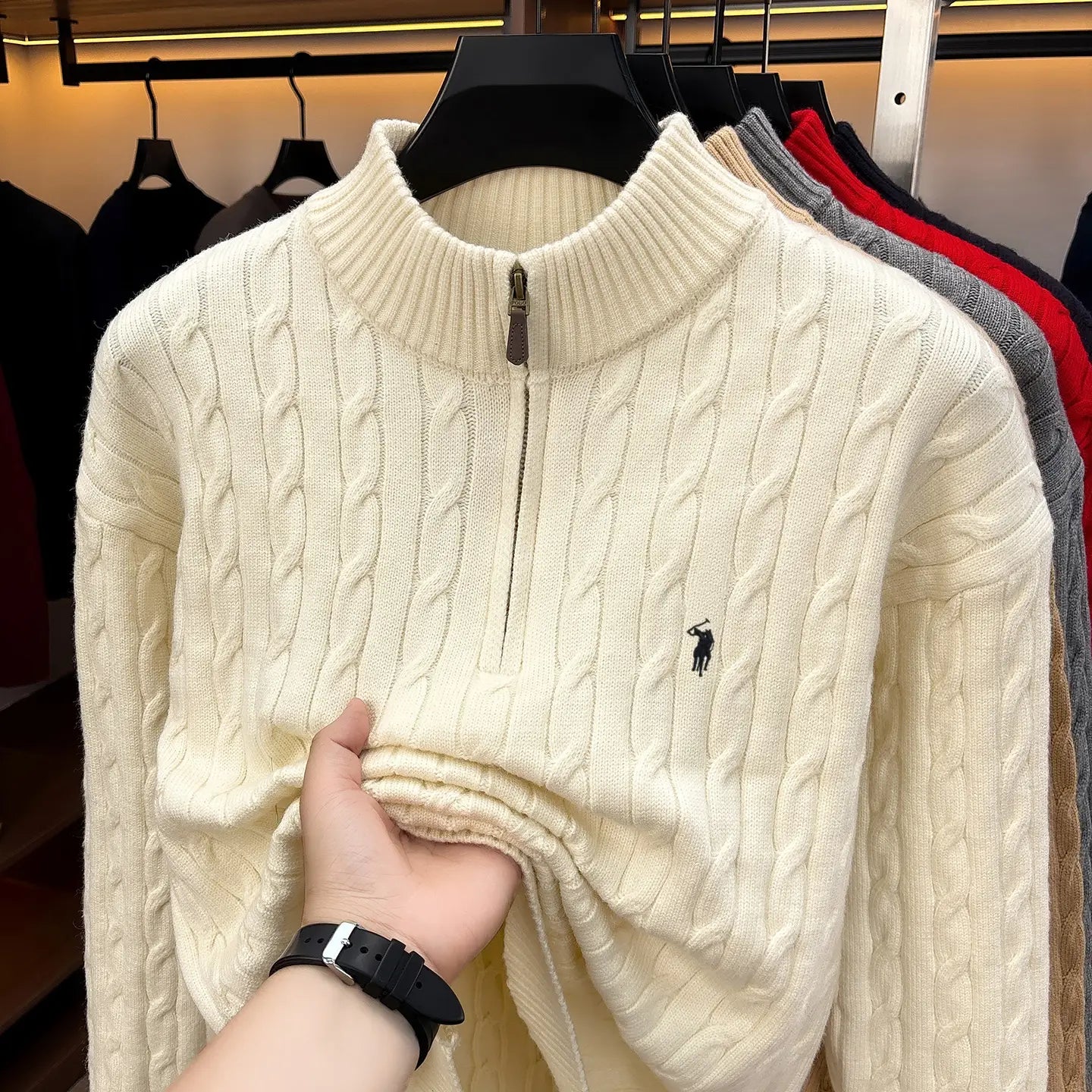 Herren-Designer-Sweater aus cremefarbenem Zopfmusterstrick mit halbem Reißverschluss, mit kleinem schwarzem besticktem Polo-Spieler-Logo auf der Brust.