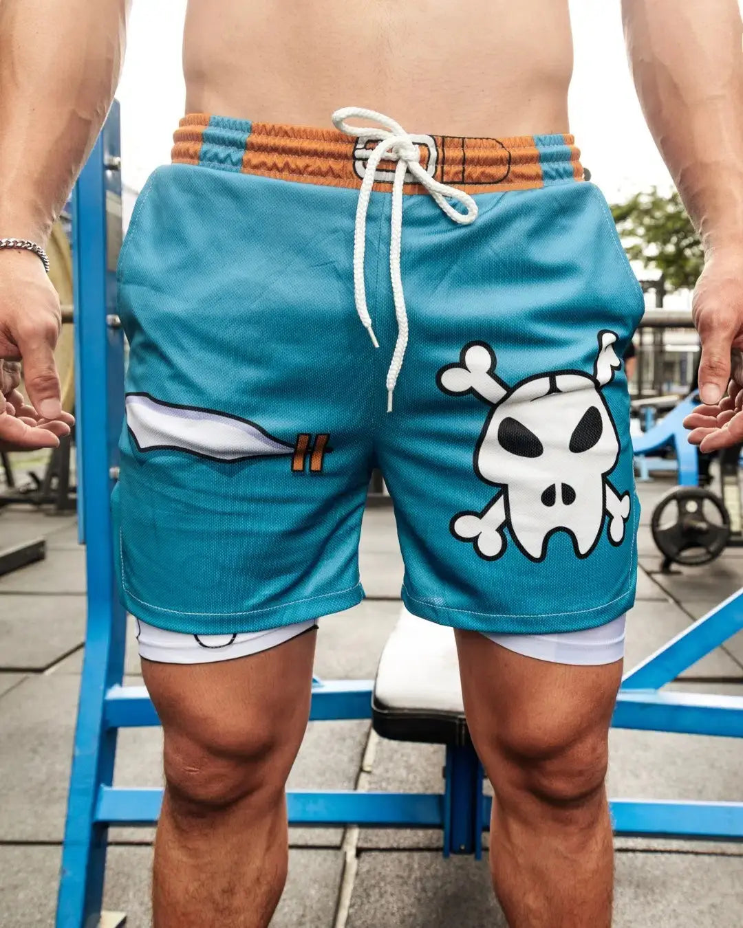 pantalones cortos de gimnasia turquesa Digimon Bandai Weregarurumon con un gráfico de calavera y tibias cruzadas estilo caricatura, cinturilla blanca ajustable con cordón y diseño en capas con pantalones interiores blancos lisos.