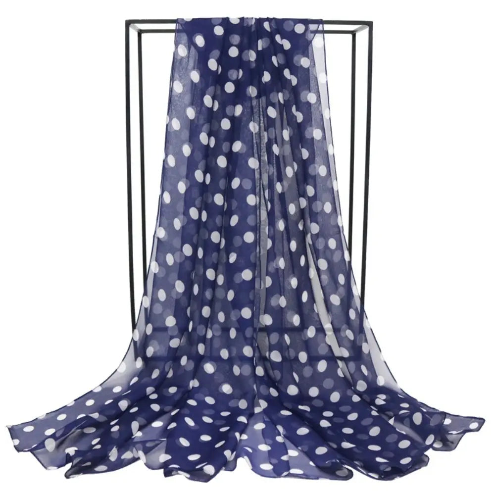 A navy blue sheer silk polka dot head wrap scarf displayed on a black metal rack.