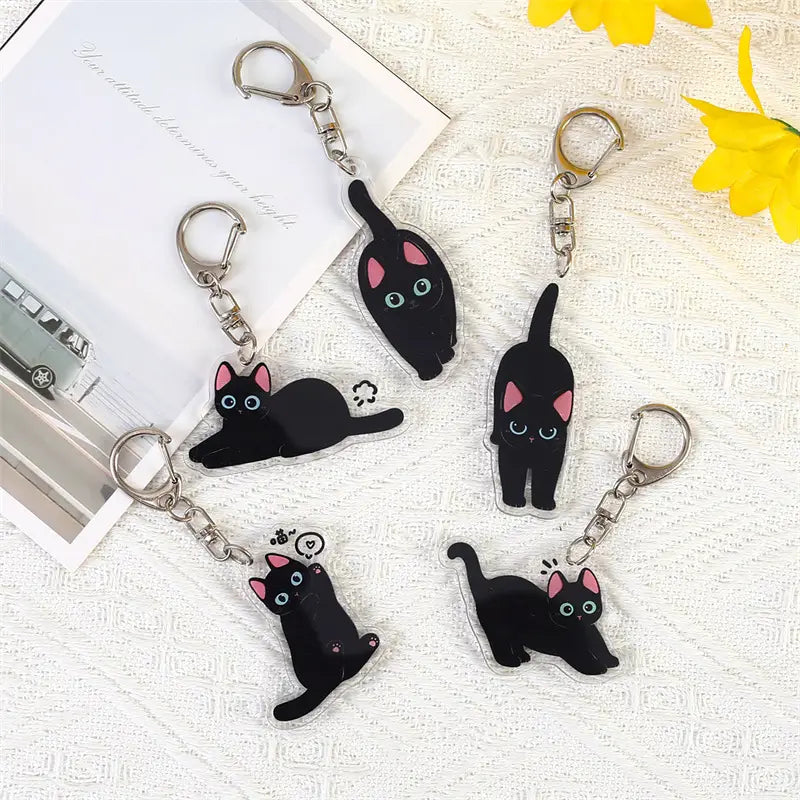 Black cat acrylic keychain featuring cartoon animal design with pink inner ears and blue eyes made of clear acrylic with silver metal clasps for use as a bag charm.