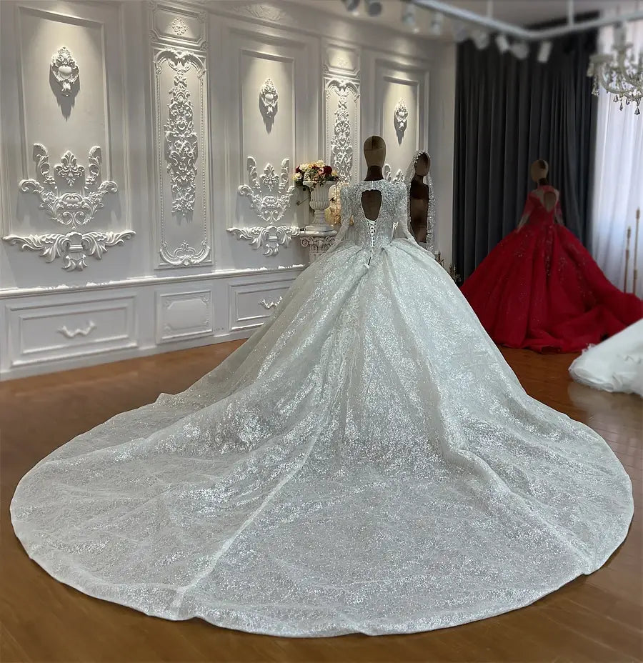Robe de mariée sur mesure à manches longues en dentelle et jupe en forme de cloche, argenté scintillant, avec des détails de dentelle complexes et une traîne volumineuse atteignant le sol.