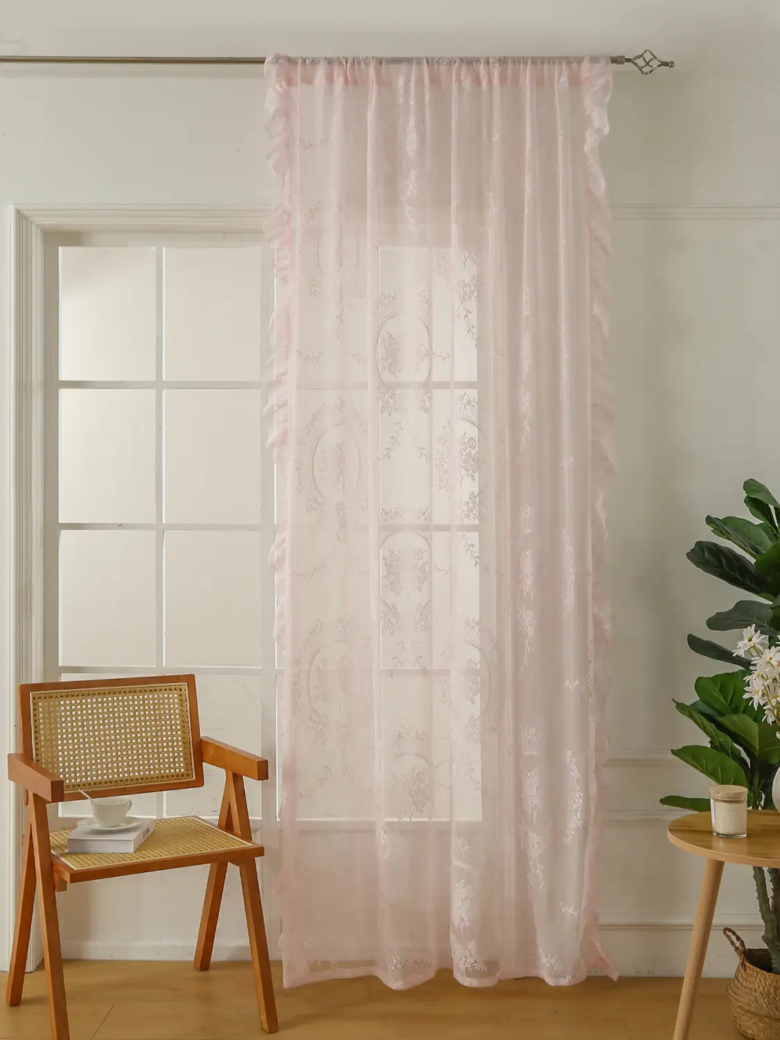 Una cortina de encaje rosa claro delicada con bordadura floral sutil y bordes fruncidos, colgada con elegancia de una barra de soporte para espejo circular con bolsillo para la barra
