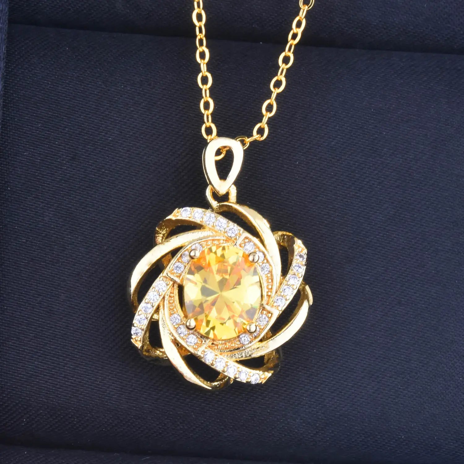 Collier pendentif moulin à vent en citrine doré comportant une pierre jaune centrale entourée de bandes dorées tourbillonnantes, incrustées de diamants transparents.