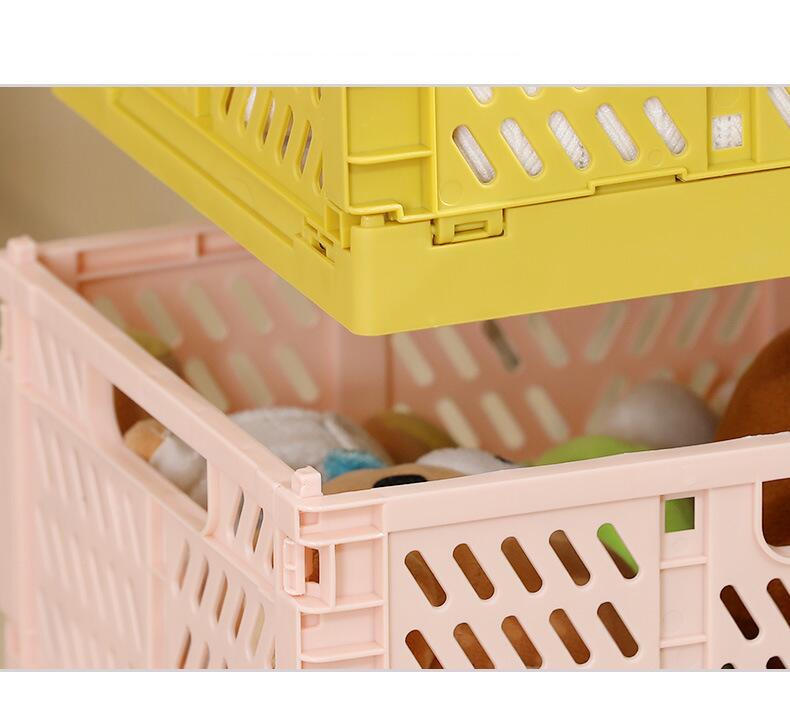 a stack of two foldable storage baskets made of plastic lattice crates in pale pink and bright yellow with collapsible grid patterns and elongated slotted openings