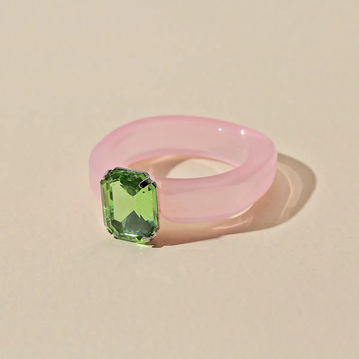 A colorful resin crystal geometric ring for women featuring a translucent pink band with a prominent emerald-cut green gemstone set in silver-toned metal.