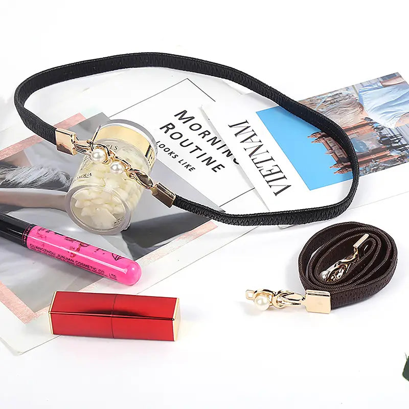 Schwarzer elastischer Choker für Damen mit goldfarbenen Beschlägen und einem klaren zylindrischen Anhänger, der weiße Perlen enthält, als Bestandteil eines Perlen-Schnallen-Taillegürtels für Frauen.