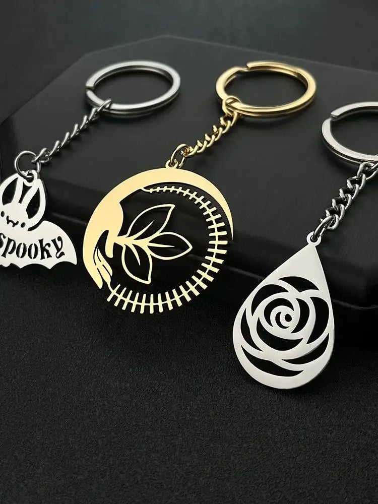 custom engraved metal keychains featuring three metallic designs including a spooky bat charm, a stitched crescent moon with leaves, and an intricate rose cutout for personalized gifts.