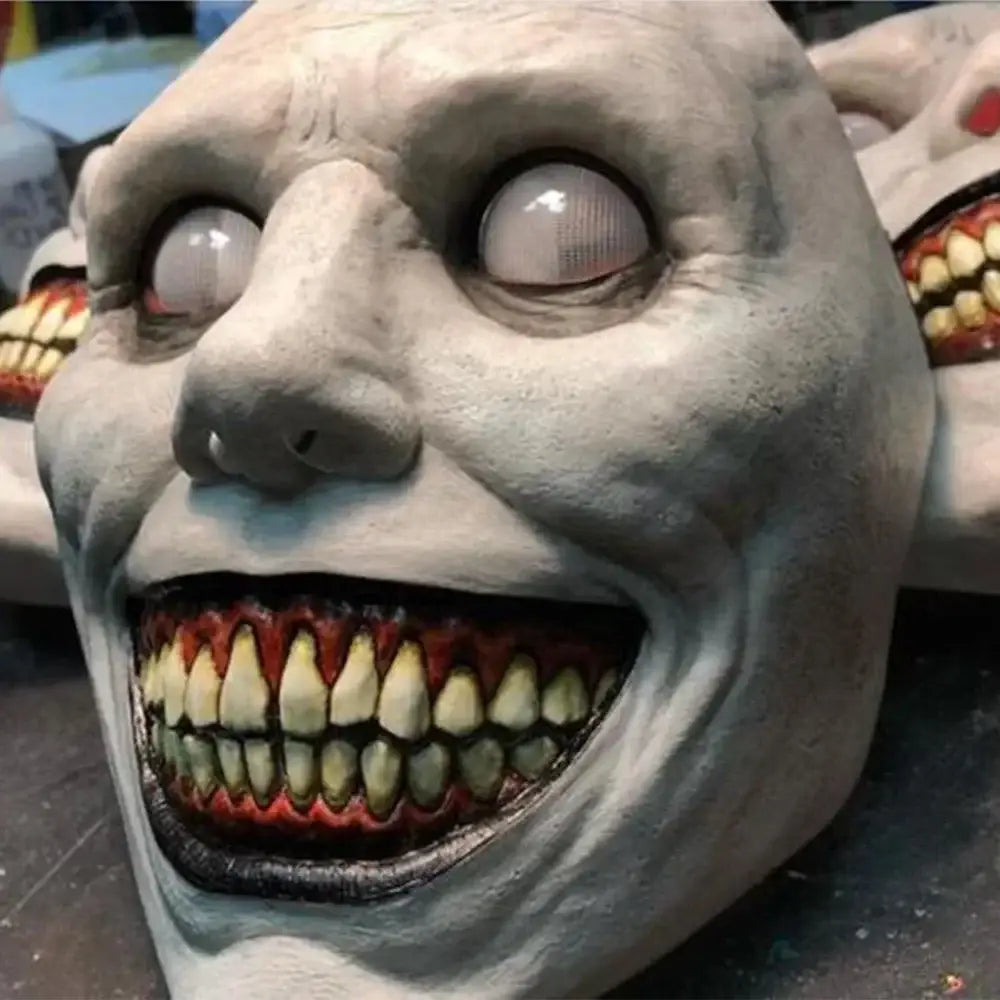 a creepy halloween resin horror mask full face costume accessory featuring a grotesque pale gray latex design with exaggeratedly wide eyes and a gaping mouth filled with yellowed teeth set against a red interior.