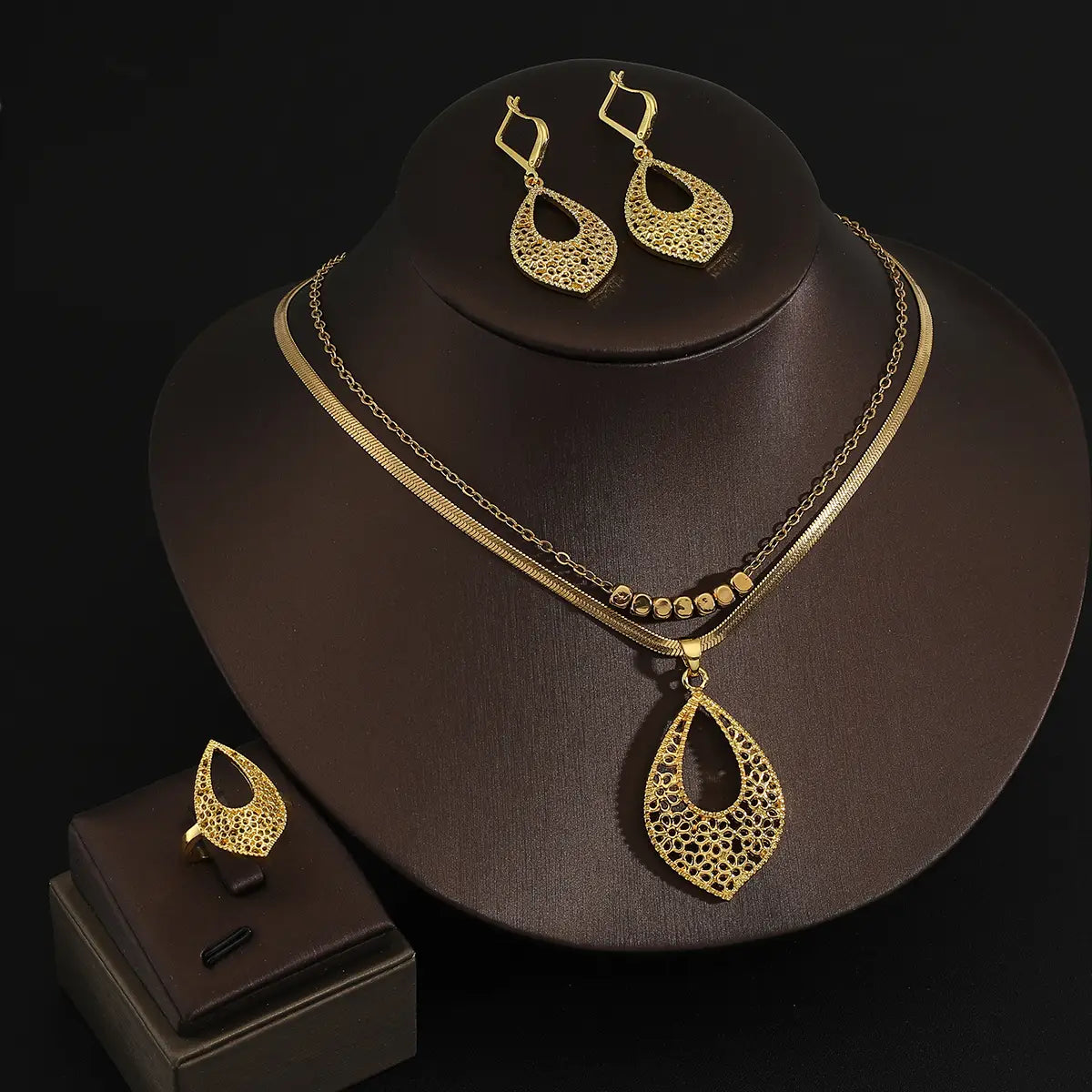 Juego de joyería de acero inoxidable color dorado para mujeres, con un collar con dije de forma de lágrima y un diseño calado de filigrana intrincada, así como aretes y anillo a juego.
