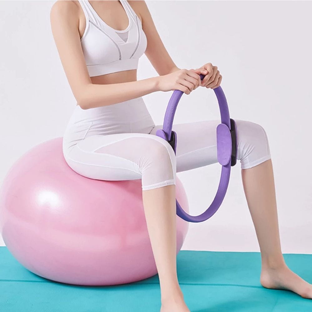 Purple Pilates Ring fitness magic circle with black adjustable straps resting on a pink exercise ball for yoga equipment and workout routines.