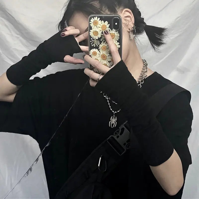 a phone case with a glossy finish adorned with white daisies featuring gold centers displayed alongside striped knit fingerless arm warmers