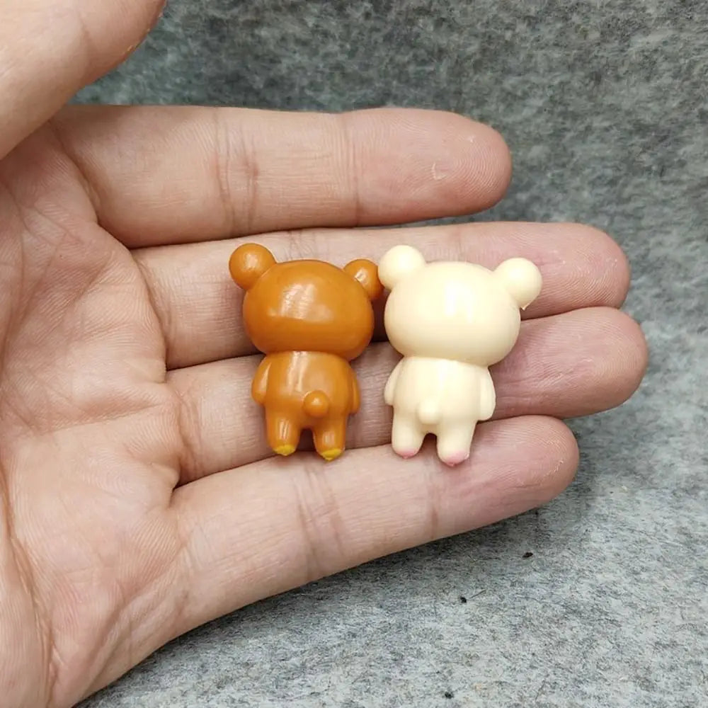 Two miniature rilakkuma bear keychain pendants in warm orange and creamy off-white, made of smooth plastic with rounded ears and simple stitched details.