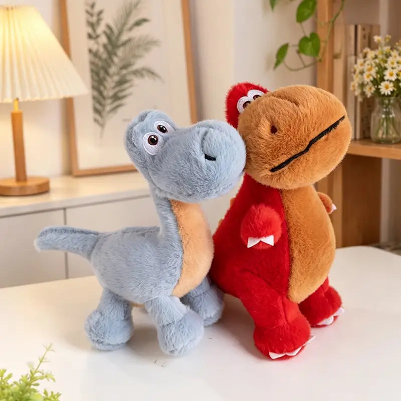 Deux jouets peluches de dinosaure colorés en bleu clair avec un ventre beige et en rouge avec un ventre brun, présentant des corps en tissu souple et des détails faciaux brodés.