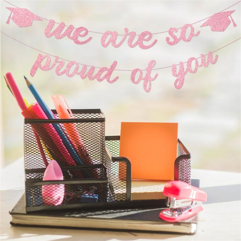 black mesh desk organizer with multiple compartments holding pencils markers and office supplies next to a pink glitter graduation proud of you banner