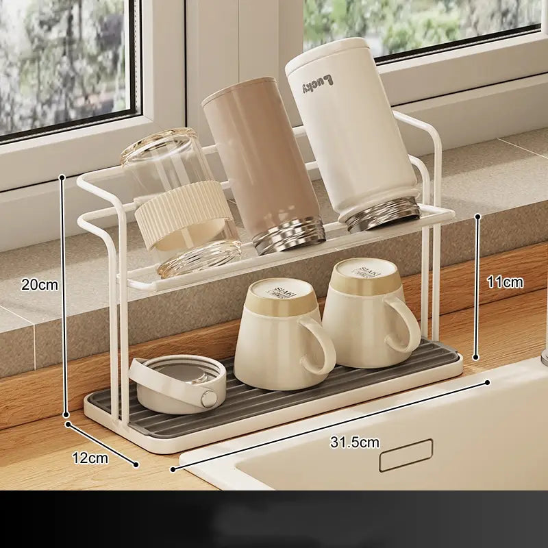 White two-tiered stainless steel mug and cup storage rack with a gray textured base and metal frame holding various mugs and tumblers.