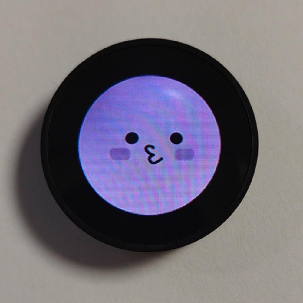 Circular black mini gadget smart desktop companion with a glowing purple screen displaying a cute cartoon face and included data cable.