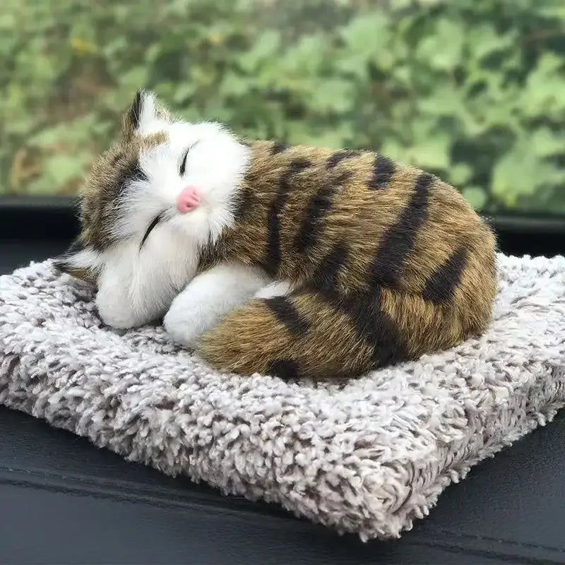 Adorable brown and black striped simulated sleeping cat plush toy with white fur on face paws and belly resting on a textured gray cushion with sound feature.