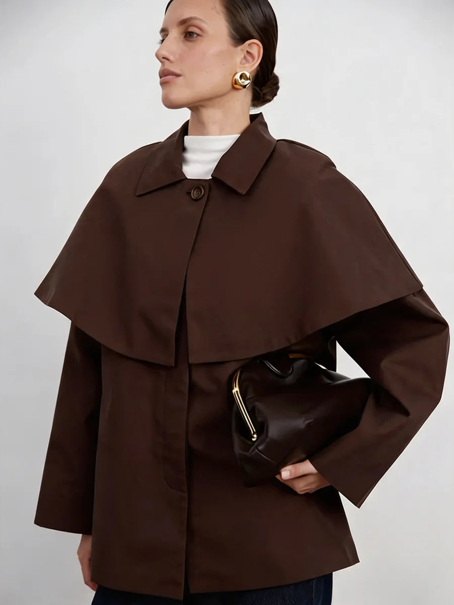 Abrigo tipo gabardina marrón de mujer ajustado con cinturón y superposición de capa, con cuello estructurado y mangas amplias por capas.