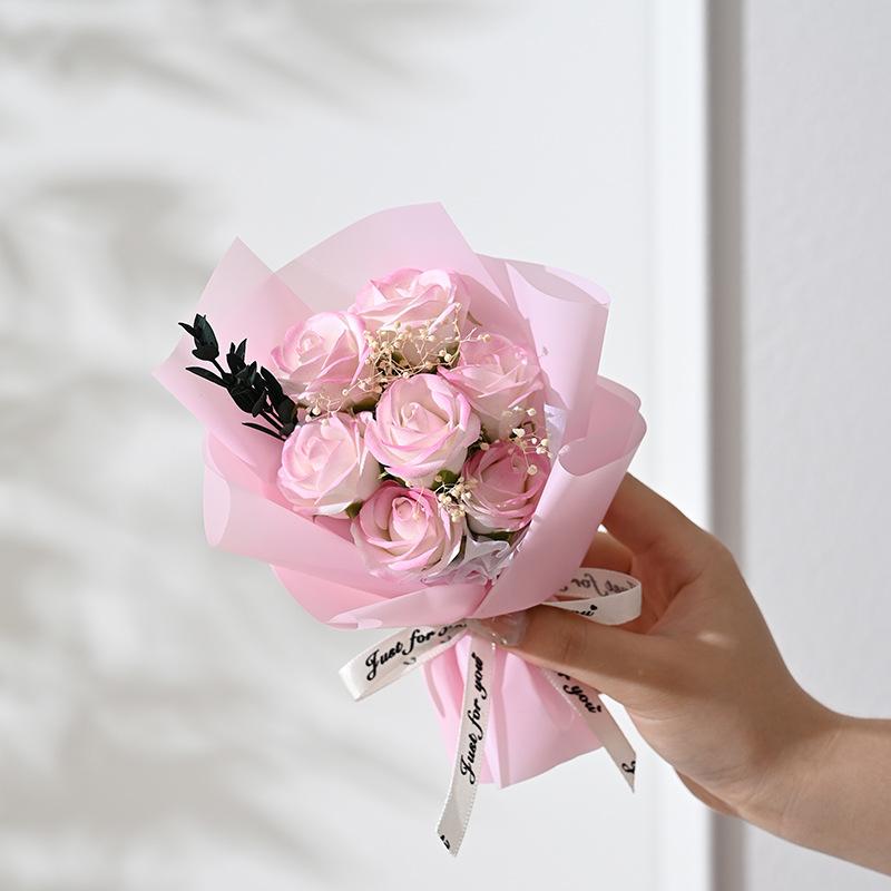 a delicate artificial rose flower bouquet of soft pink preserved roses wrapped in matching translucent paper and tied with a white ribbon for gifts