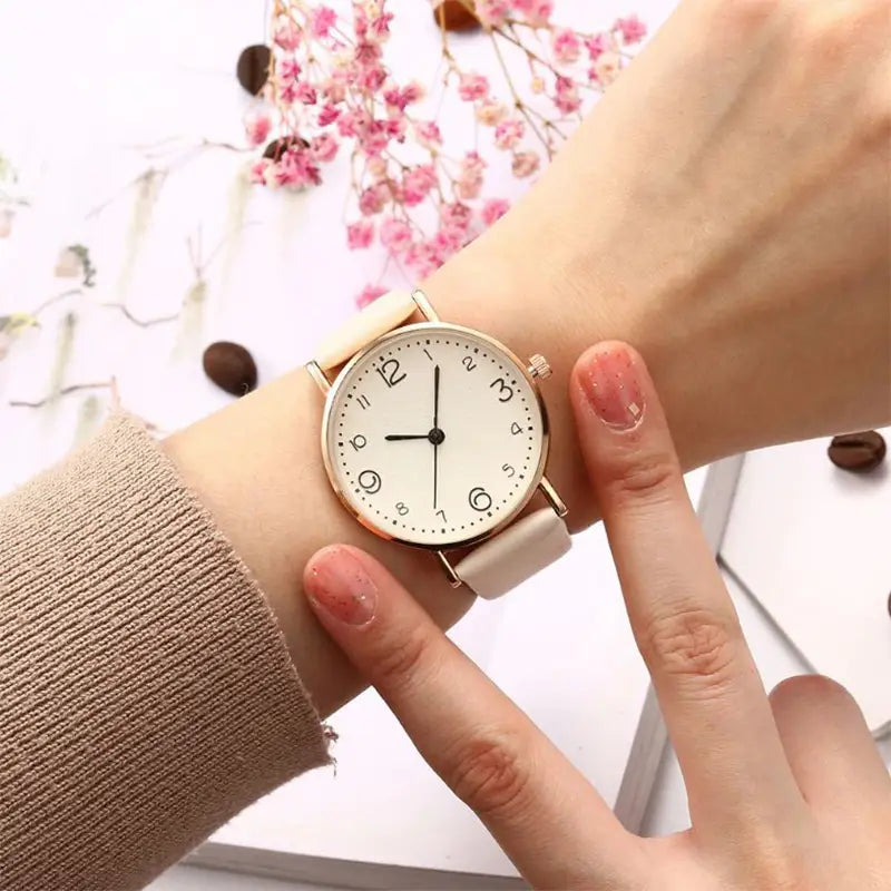 A rose gold leather casual watch with Arabic numerals featuring a minimalist white dial and cream-colored leather strap worn elegantly on a wrist.