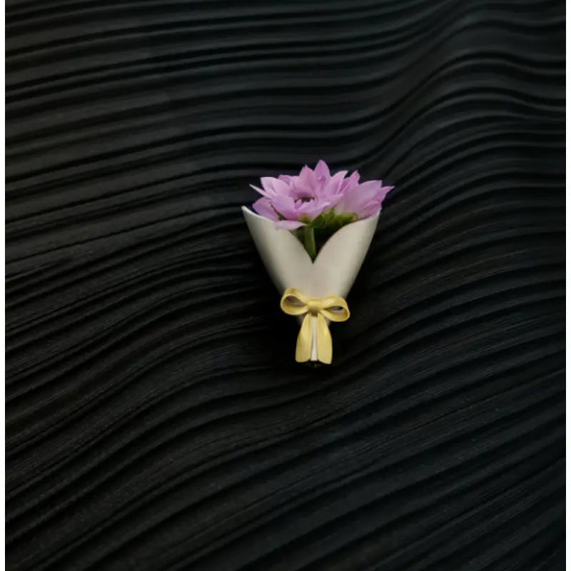 Ein kreatives Corsage-Zubehör in Form einer zarten rosafarbenen Blumen-Broschennadel, umwickelt mit cremefarbenem Papier und mit einer gelben Schleife gebunden.