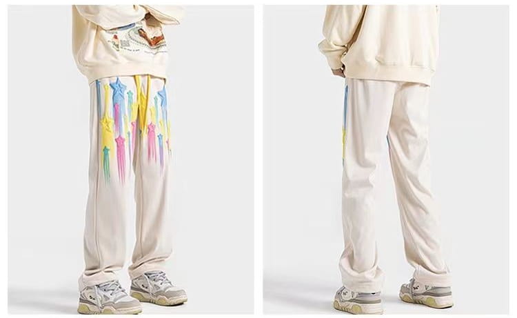 Cream-colored men sweatpants made of soft fabric featuring vibrant dripping rainbow paint splashes down the outer legs in the rainbow star graphic design.