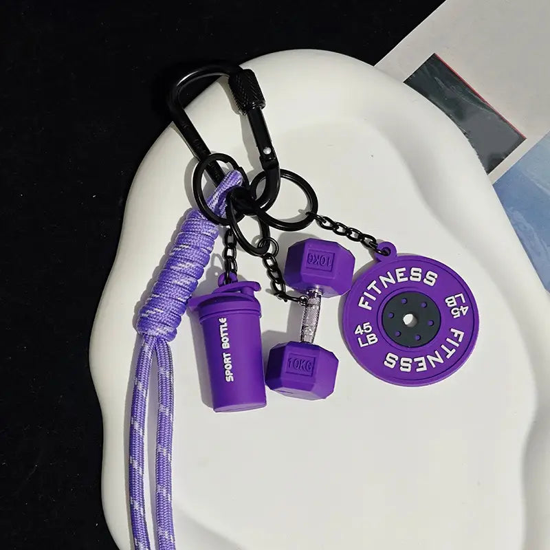 Un porte-clés de fitness violet comprenant des breloques d’haltère, de disque de poids et de bouteille shaker comme accessoire de sac de sport.