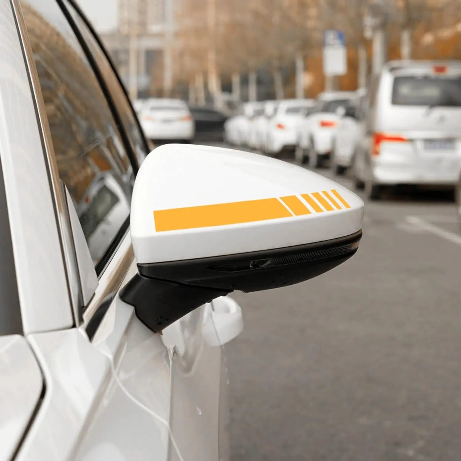 Miroir latéral de voiture blanc comportant un lot d’autocollants vinyle rayés orange audacieux, avec trois lignes parallèles sur l’ensemble de sa surface.