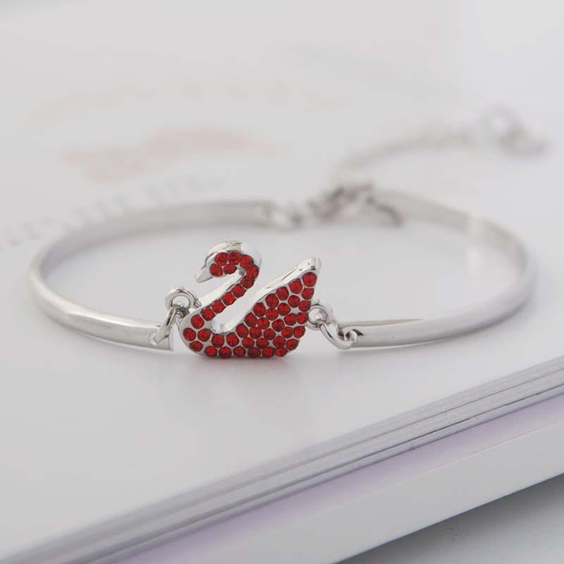 Bracelet jonc à tonalité argent, avec une breloque centrale de cygne sertie de cristaux rouges.