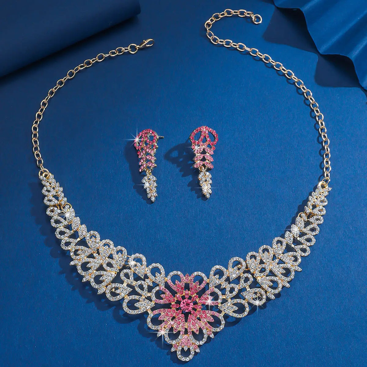 Un ensemble de bijoux en forme de fleur en cristal rose plaqué or à la finition ton or, comprenant un collier au design délicat façon dentelle, orné de cristaux clairs et roses, accompagné de boucles d’oreilles assorties.