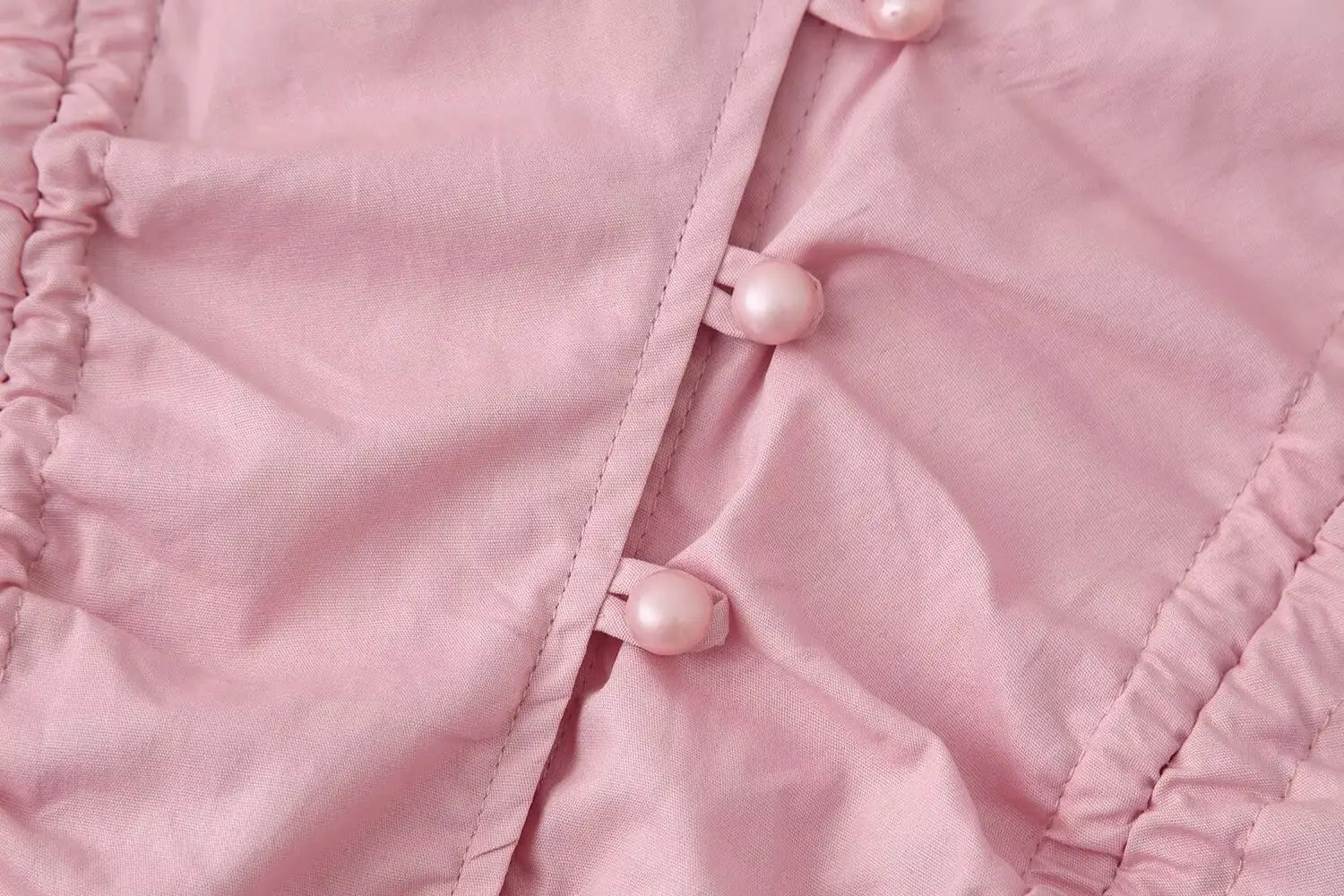 women slim fit long sleeve round neck top in pink satin-like fabric featuring pearl buttons and ruched detailing highlighting the slim-fit design and round neckline.
