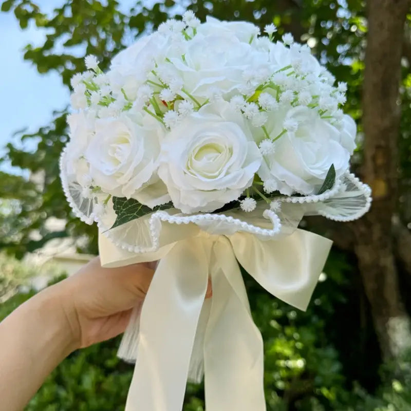 Elegant white silk rose wedding bouquet featuring delicate lace trim pearls and a cream satin ribbon bow.