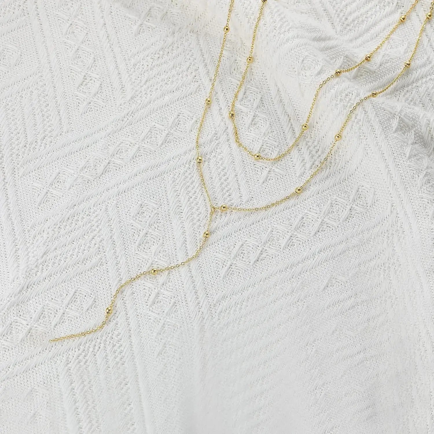 Un collier en couches d’or délicat pour femmes, présentant des chaînes au ton or fin avec de petites perles sphériques.
