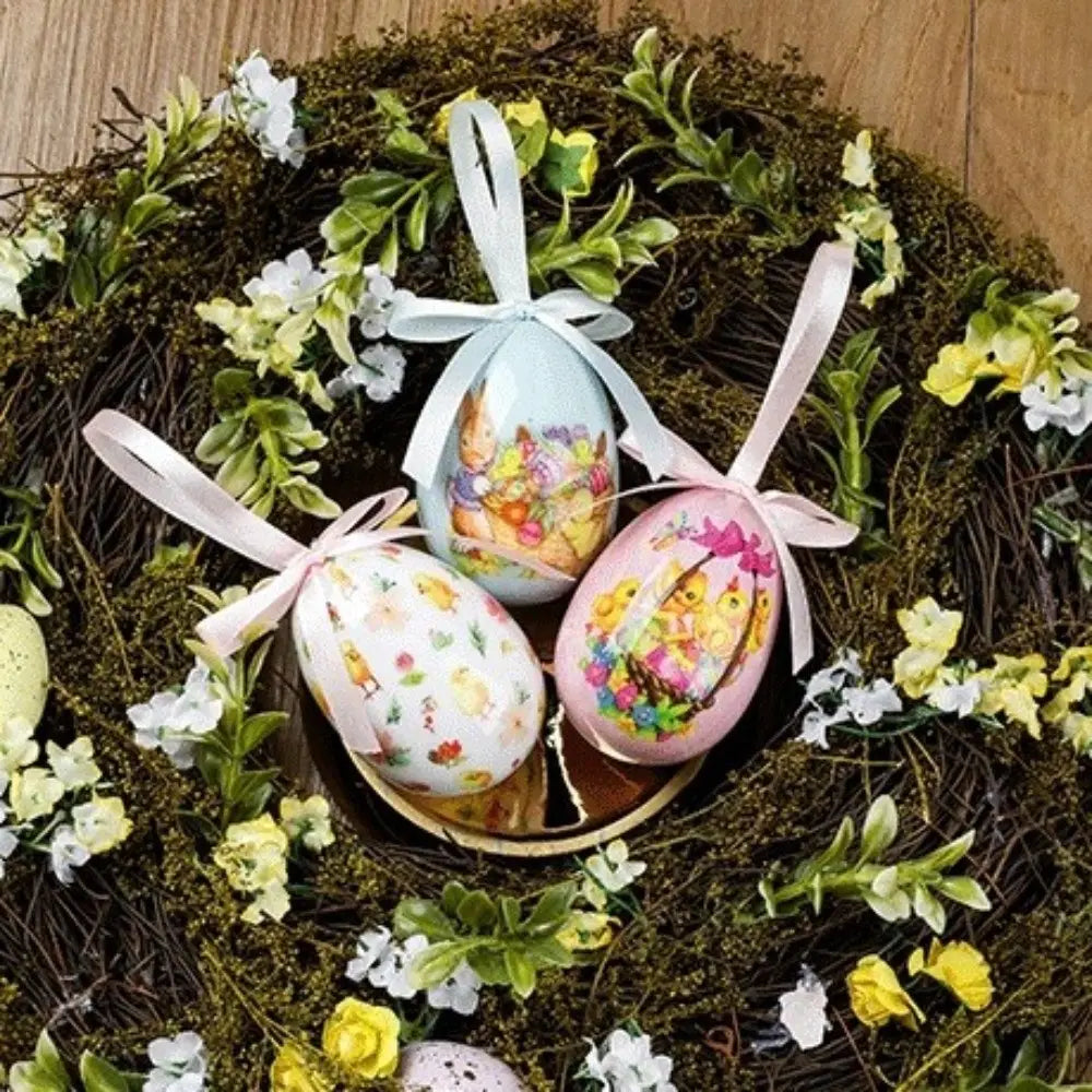 trois œufs de Pâques en mousse suspendus décoratifs, décoration artisanale florale, présentant des couleurs bleu pastel, rose et blanc, avec des illustrations colorées de lapins et de poussins et des rubans délicats en satin.