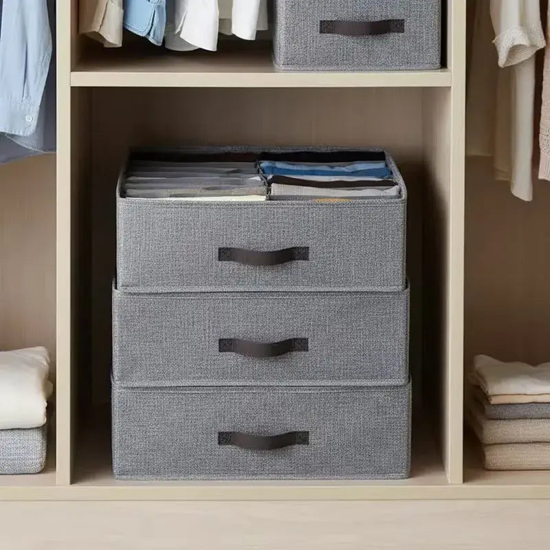 boîte de rangement pliable pour vêtements avec tiroirs en tissu gris superposés et poignées noires, organisant proprement des vêtements pliés dans un placard.