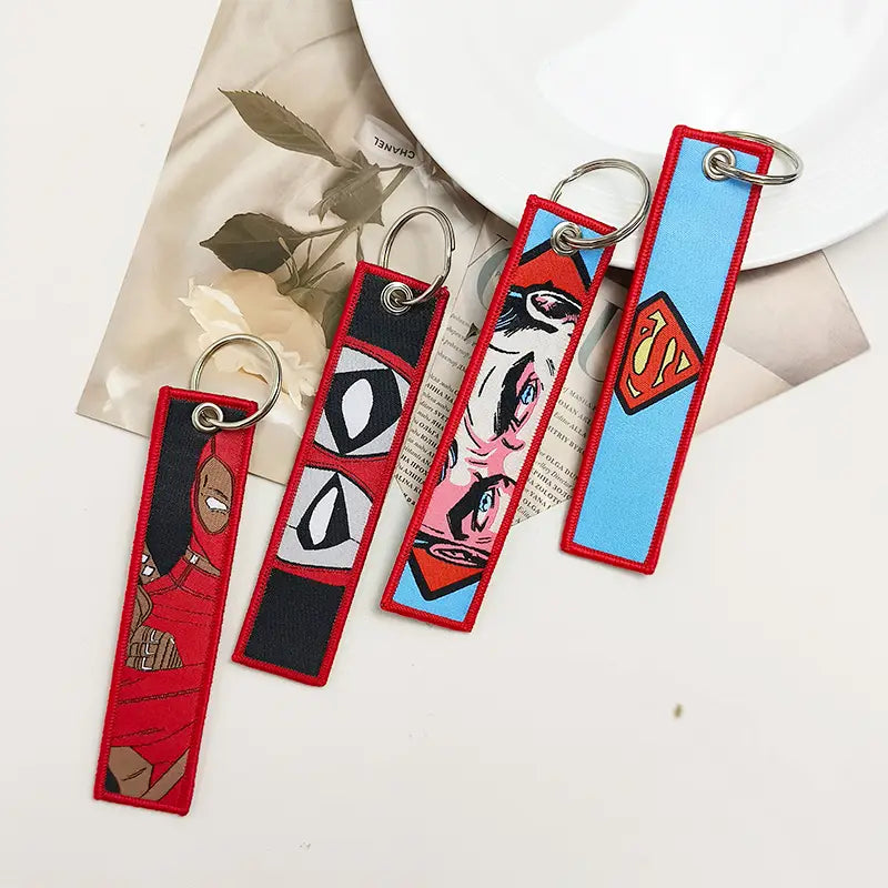 four rectangular embroidered keychains with red borders featuring superhero designs including deadpool and superman from the superhero embroidered keychain set anime key lanyard