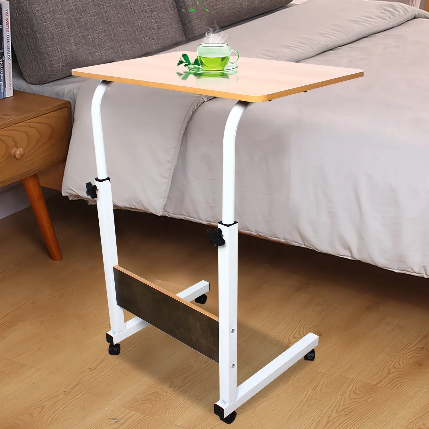 Tablette roulante pour ordinateur portable à hauteur réglable, avec structure en métal blanc, plateau en bois clair et roues pivotantes noires, conçue pour une utilisation au chevet.