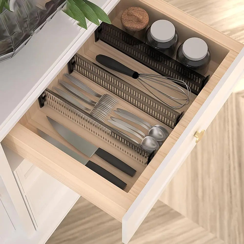 Black plastic utensil organizer with slotted compartments holding knives forks spoons and a whisk designed as an expandable clear plastic drawer divider adjustable organizer.