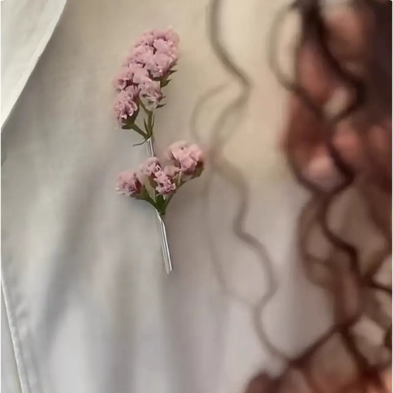 Eine zarte rosa getrocknete Blumen-Broschennadel mit einem schlanken silberfarbenen Metallstiel, gestaltet als kreatives Corsage-Zubehör.