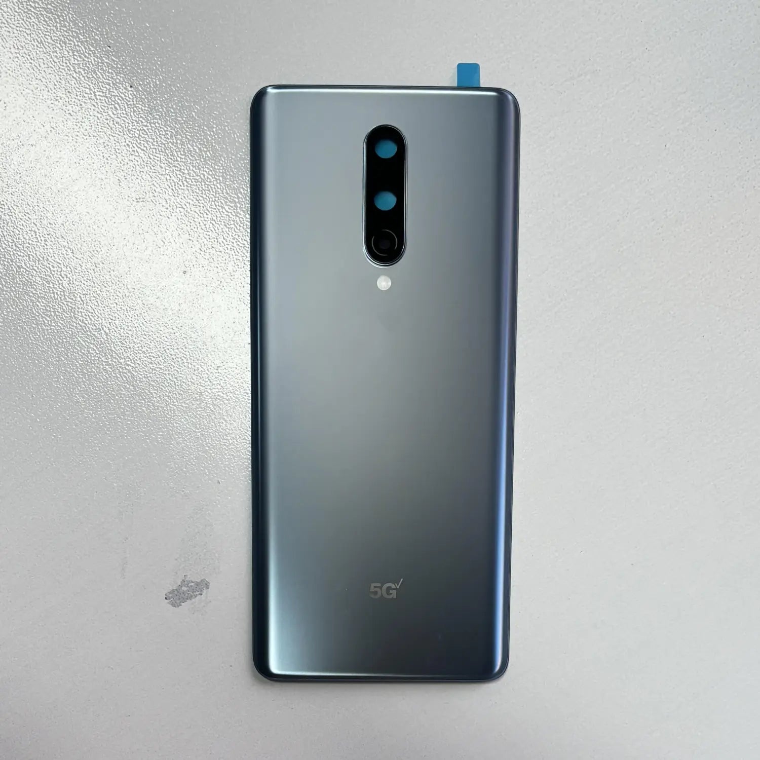 Die Rückseitenverkleidung eines eleganten Smartphone-Oneplus 8 mit silbernem Farbverlauf und vertikalem Triple-Kamera-Array, versehen mit 5G-Kennzeichnung, ausgestattet mit einer Akkufachabdeckung aus hochwertigem Gorilla-Glas modname=ckeditor.