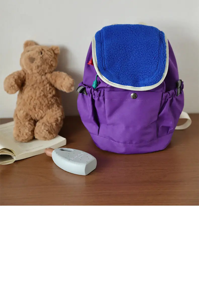 Leichter Fuzzy-Rucksack für Kinder in Lila mit einer blauen Fleece-Klappe und weißer Verzierung, entworfen als Kindergartentagesrucksack.