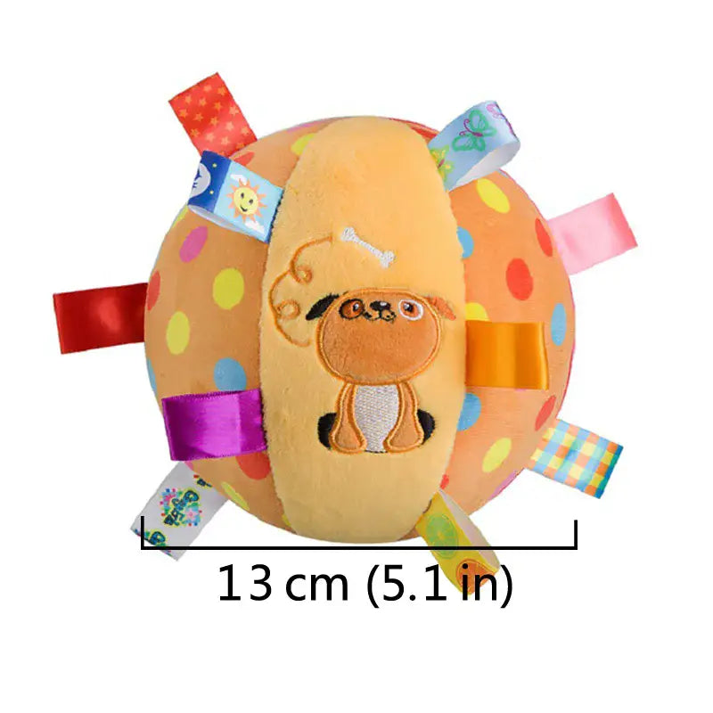 Un suave balón interactivo de peluche color naranja claro con lunares, que incluye la cara de un cachorro cosida y etiquetas de tela coloridas con un asa para facilitar el juego.