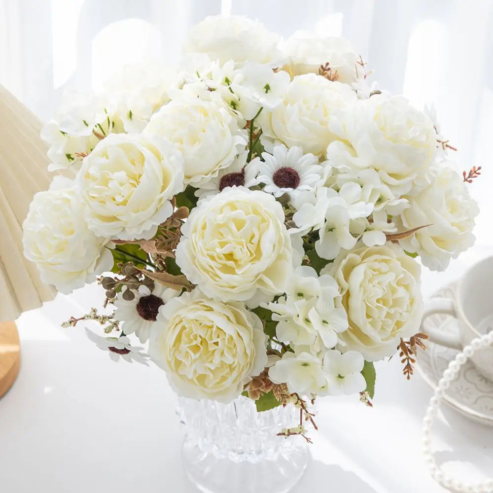 ein zarter Strauß aus künstlichen weißen Rosen und Gänseblümchen, in einer klaren facettierten Glasvase für die Wohnraumdekoration angeordnet