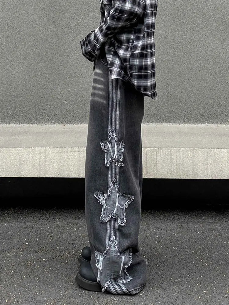 jeans en denim gris foncé style Y2k baggy délavé et déchiré, avec une rayure verticale de patchs en forme d’étoiles délimitées en blanc, délavés, descendant le long de la jambe extérieure