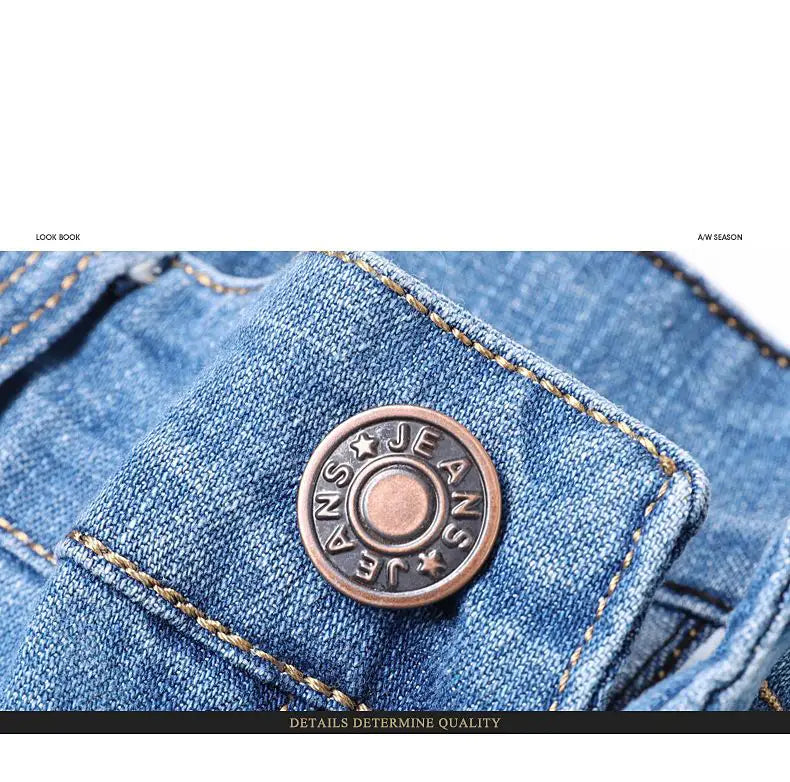 a circular bronze-colored metal button engraved with jeans and star motifs set into blue denim fabric of men’s stretch cotton straight casual trousers