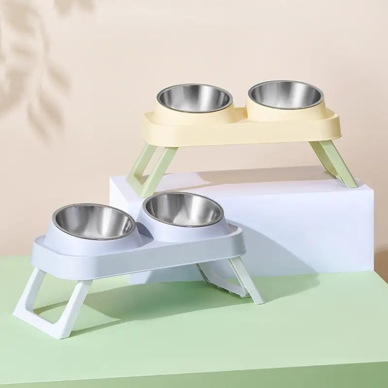 Elevated stainless steel pet feeder with tilt bowls featuring two-tone pastel yellow and light blue plastic bases and stainless steel bowls.