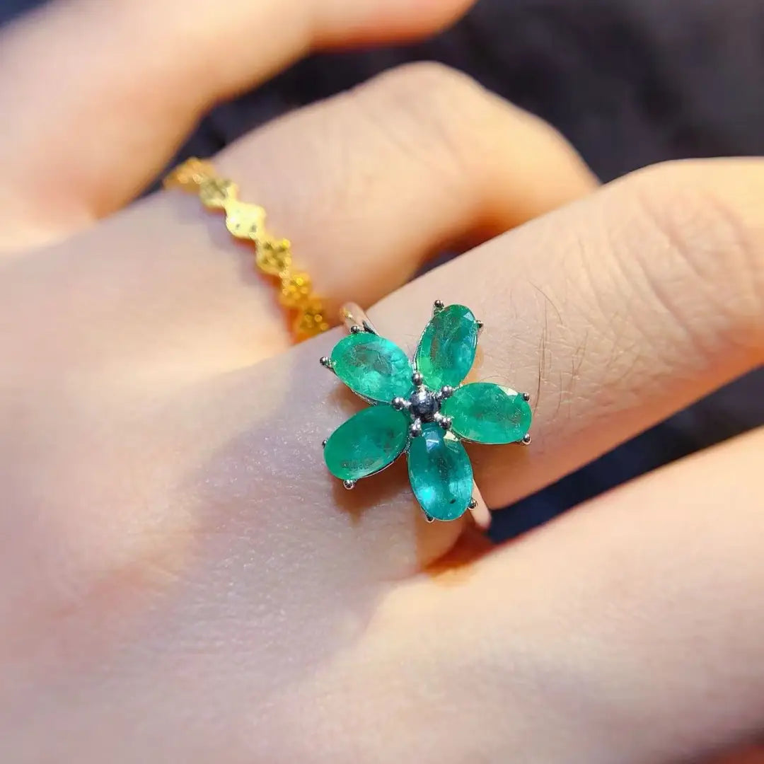 Ein Smaragdblumen-Silberring mit einem kräftig emeraldgrünen Blumendesign, bestehend aus fünf oval geschliffenen Steinen und einem zentralen Diamant-Akzent, der in einem zarten silberfarben wirkenden Band eingefasst ist.