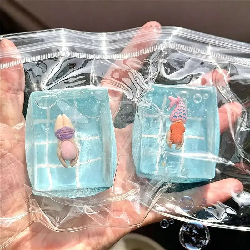 deux cubes sphériques translucides bleu clair à faible rebond, visqueux et lents, chacun contenant une mini figurine de nageur et une sirène portant des maillots colorés, vus de face